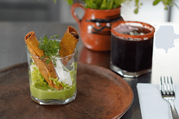 taquitos plated in a glass cup with salsa